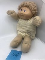 Front view of 1982 Cabbage Patch Kid doll seated wearing cream-colored elephant jumpsuit with blue eyes and light brown yarn hair.