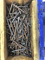 Close-up of a large quantity of old square head and regular nails inside a lined box showing rusted and aged condition.