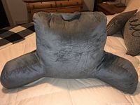 Front view of the grey plush backrest pillow with large side supports set on a bed.