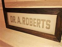 Front view of milk glass sign reading 'DR. A. ROBERTS' set in a wooden frame.