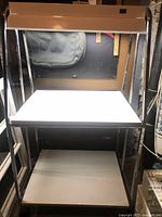 Front view of grow plant cart with fluorescent light turned on showing upper and lower shelves and metal frame