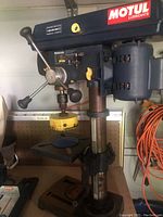 Full view of Mastercraft 10 inch bench drill press showing mounted 4 inch yellow hole cutter bit and three-pronged drill handles.
