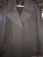 Front view of grey men's trench coat jacket on wooden hanger showing double-breasted buttons, epaulets, and flap pockets
