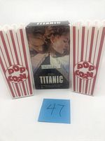 Front view of two plastic popcorn containers flanking the Titanic VHS box set with movie characters on cover
