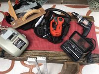 Photo showing the overall tool lot including Black & Decker Zip Saw in case, heavy duty drill, socket set, sharpener, mitre box, screwdriver holder, appliance rollers, and wooden box all placed on a wooden pallet with red mat.