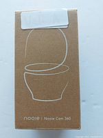 Front of brown box packaging showing simple line art of Nooie Cam 360 camera and branding.