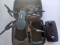 Foldable drone with extended arms, remote controller, and carrying case with visible compartments and batteries.