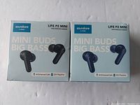 Photo of the front of two boxed sets of Soundcore Life P2 Mini earbuds, one black and one blue, showing product features like AI-enhanced calls and 32 hours playtime.