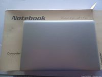 Closed silver notebook laptop atop original beige box with 'Notebook' labeling.