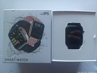 Smart watch in white box with the watch displayed in the inner compartment and the box lid showing images of the watch with different faces and fitness information.