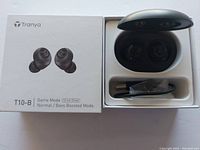 Tranya T10-B wireless earbuds in open charging case with USB charging cable. Product box shown with labeling indicating Game Mode Normal/Bass Boosted Mode and 12mm drivers.