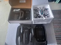 Photo showing three drones: one black foldable drone, one white drone with propeller guards in foam, and a smaller black drone in a box.