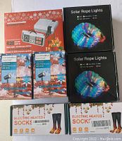 Photo shows all items in the lot: Nintendo 8-bit Anniversary Edition mini console box, two solar rope lights boxes, two cool white/blue snowflake light boxes, and two electric heated socks boxes.