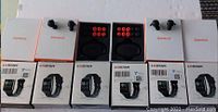 Overhead view of six Lesstar smart watch boxes in bottom row and six Zemkot wireless earbud boxes (two opened to show charging cases and extra tips) in top row