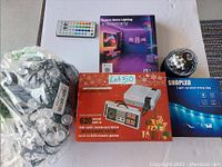 Top view of the lot showing all items: boxed 660 Mini Anniversary Game, modern LED strip light box and remote, disco ball light, and a bag of Christmas string lights.