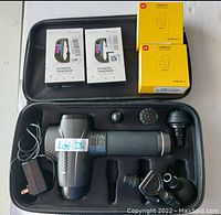 Top down view of lot showing handheld massager with interchangeable heads inside a carrying case along with two boxed fitness tracker smart watches and two boxed UMIDIGI AirBuds U wireless earbuds.