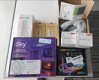Photo shows the mixed lot with boxed JessShines Sky Lite projector night light, two LED headlamp boxes, KIKO LED strip light box, two heat hand warmer boxes, a white desk lamp in plastic bag, and a smart plug instruction manual.