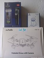 Photo displays three boxed items: professional hair clipper, dog collar, and foldable drone with camera.