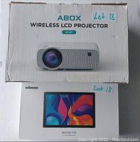 Photo showing both the Winnoyo WinTab P20 tablet box and the ABOX Wireless LCD Projector box stacked, each labeled Lot 18.