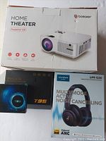 Photo shows Bomaker Projector C9 box on top, T95 TV Box boxes to the left, and Anker Soundcore Life Q30 headphones box to the right on a white surface.