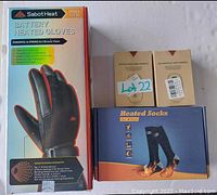 Box of Sabot Heat battery heated gloves, two boxes of rechargeable hand warmers labeled Lot 22, and a box of heated socks displayed on a white surface