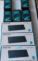 Photo showing one full-size Omoton wireless keyboard box and five mini wireless keyboard boxes, all sealed and new.