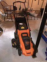 Front view of Black & Decker electric lawn mower with handlebar, orange and black body, showing front wheels and motor cover labeled 13 amp.