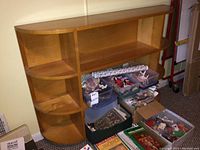 Front-facing view of the wood bookcase showing curved sides and open shelving space with items around base.