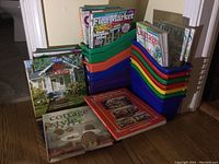 12 plastic magazine storage containers and various magazines and books related to homes, cottages, and DIY.
