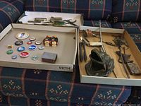 Photo showing many vintage buttons themed around politics and locations, a few vintage tools and items including a plastic toy, metal matchbox, bottle opener, nutcracker, corkscrew, and a mail scale.