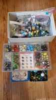 Collection of marbles in various containers shown on wooden floor.