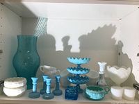 Shelf with various milk glass and blue glass items including vase, candlesticks, bowls, candy dish, and small jars