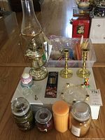 Overview of lot on table including oil lamp, brass candle holders, various candles and accessories.