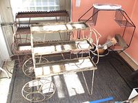 Shows three metal plant stands positioned together near a window, emphasizing size and style differences.