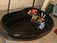 Photo showing large black plastic pond liner with various pond supplies and books inside it