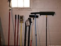 Photo shows post hole digger with red handles, three push brooms with various brush heads, and limb trimmer