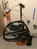 Ridgid wet/dry vacuum with attached hose and accessories, Bissell Little Green cleaner and cleaner bottle visible in background.