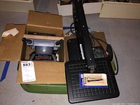 Dremel scroll saw top view with extra saw blades and partially boxed Black and Decker Workmate below.