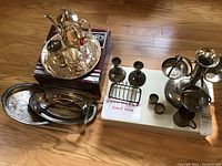 Full view of the set on the floor showing multiple silverplate items including trays, coffee set, candlesticks, toast rack, napkin rings, epergne, and ladle.