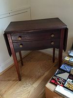 Front view of dark wooden silverware table with fold-up sides and two drawers