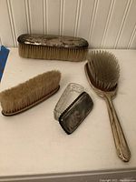 Three brushes and one lidded glass container shown together on a white surface.