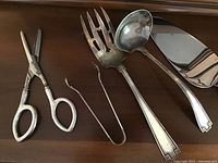 Five utensils laid on wood: scissors, tongs, serving fork, ladle, pie server