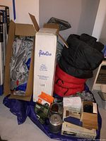 Photo of camping gear including boxes for tents, rolled sleeping bags, and some cooking items arranged on a blue tarp.