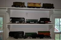 Three white shelves holding nine steel-bodied train cars of various styles and colors