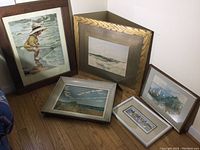 Five framed seascape and coastal wall art pieces arranged on floor and leaning against wall