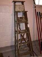 Full front view of two wooden step ladders showing paint splatters and usage wear.