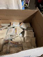 Wide view of a large cardboard box containing over 1000 individual sealed packs of crystal self-adhesive temporary tattoos in assorted styles, for body and face. Packs are plastic wrapped with backing cards visible.