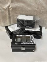 Four stacked black leatherette jewelry boxes wrapped partially in plastic with styrofoam packing inside on the top boxes.