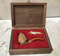 Antique Meerschaum pipe with carved detailed bowl and amber stem in wooden case with red velvet interior and small golden decorative feather/leaf.