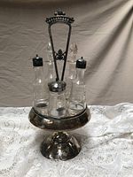 Full view of the silver plate condiment holder with five etched crystal bottles inside.